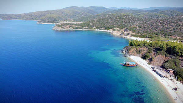 Pogled iz vazduha na plažni bar, tradicionalni brod i kristalno čisto more na obali Sitonije.